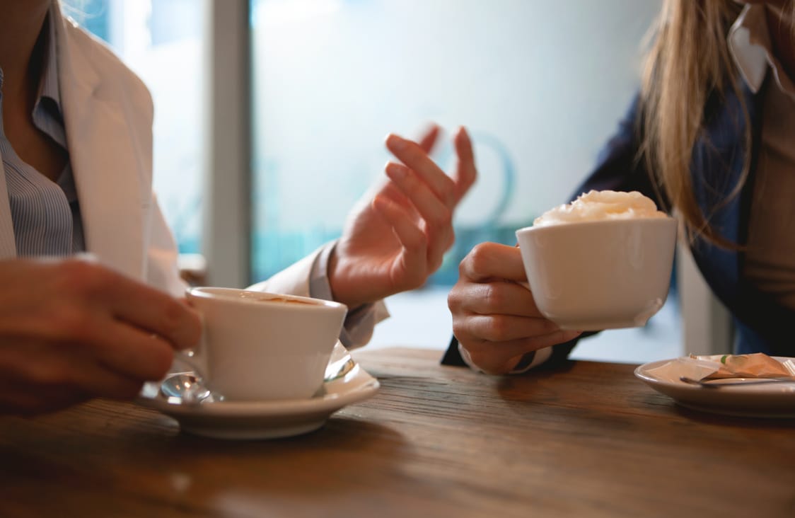 Twee mensen in gesprek aan een tafel, allebei met een kop koffie
