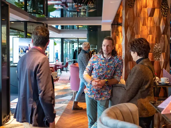 Deelnemers in gesprek in lounge, man met mondkapje achter