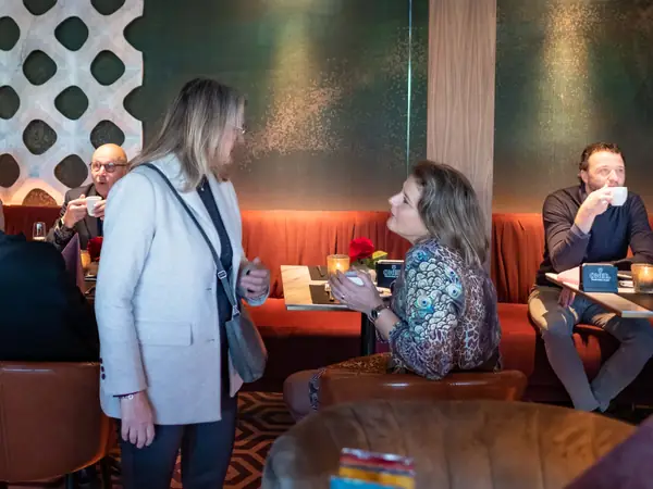 Vrouwen in gesprek bij oranje bank, man drinkt koffie