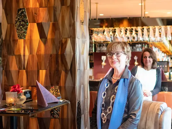 Host met blauwe sjaal glimlacht bij houten wand
