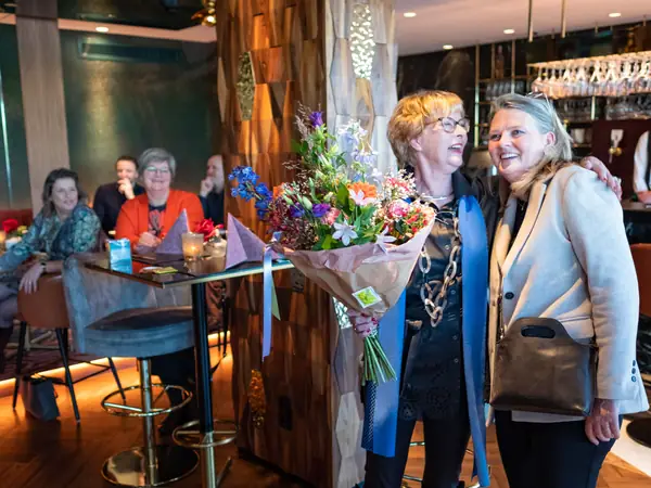 Host en vrouw lachen arm in arm met boeket, publiek lacht mee