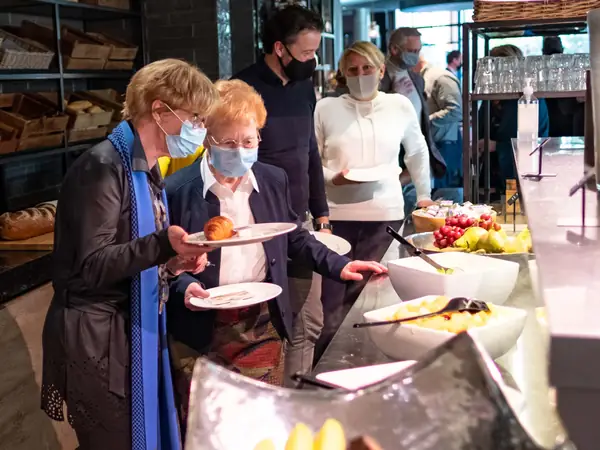 Deelnemers met mondkapjes pakken ontbijt bij buffet
