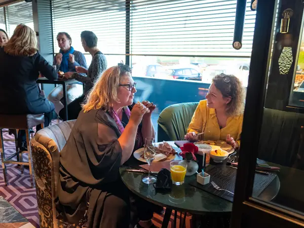 Twee vrouwen lachen samen aan ronde tafel bij raam
