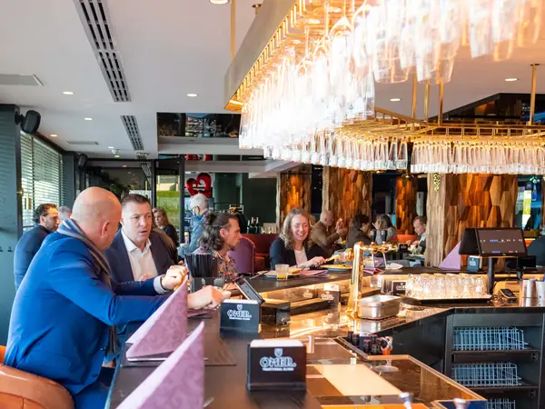 Deelnemers ontbijten aan bar onder hangende glazen