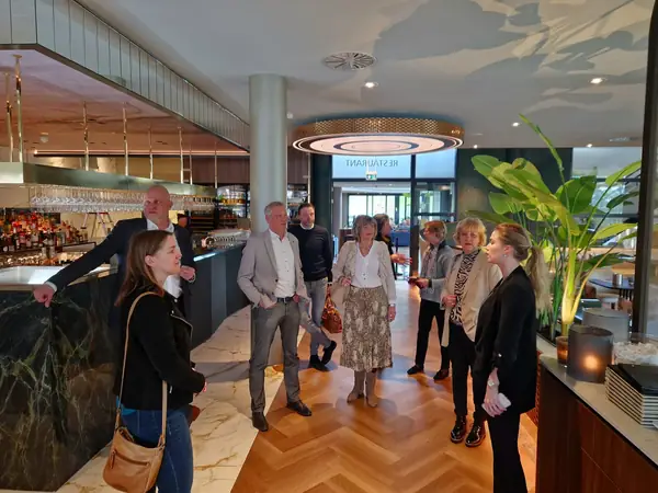 Deelnemers luisteren naar gastvrouw bij bar van restaurant